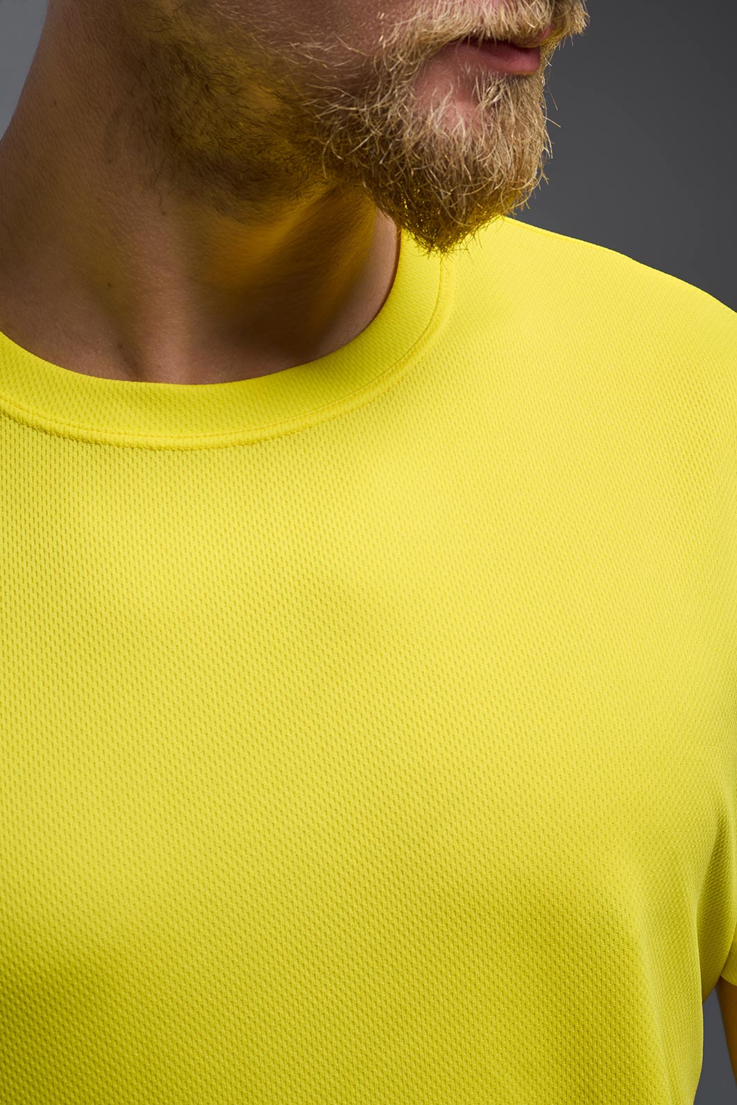 A blonde male model with a beard on a gray background, wearing the Men's Oxymesh™ Crewneck Tech Tee in the color bright yellow from a closeup collar front view. This shirt is made in the USA and is quick-drying and moisture-wicking. #color_bright-yellow