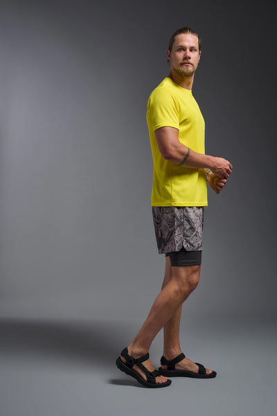 A blonde male model with a beard on a gray background, wearing the Men's Oxymesh™ Crewneck Tech Tee in the color bright yellow from a full body side view. This shirt is made in the USA and is quick-drying and moisture-wicking. #color_bright-yellow