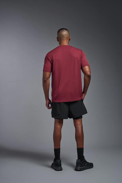 An African American male model with a beard on a gray background, wearing the Men's Oxymesh™ Crewneck Tech Tee in the color cardinal from a full body back view. This shirt is made in the USA and is quick-drying and moisture-wicking. #color_cardinal