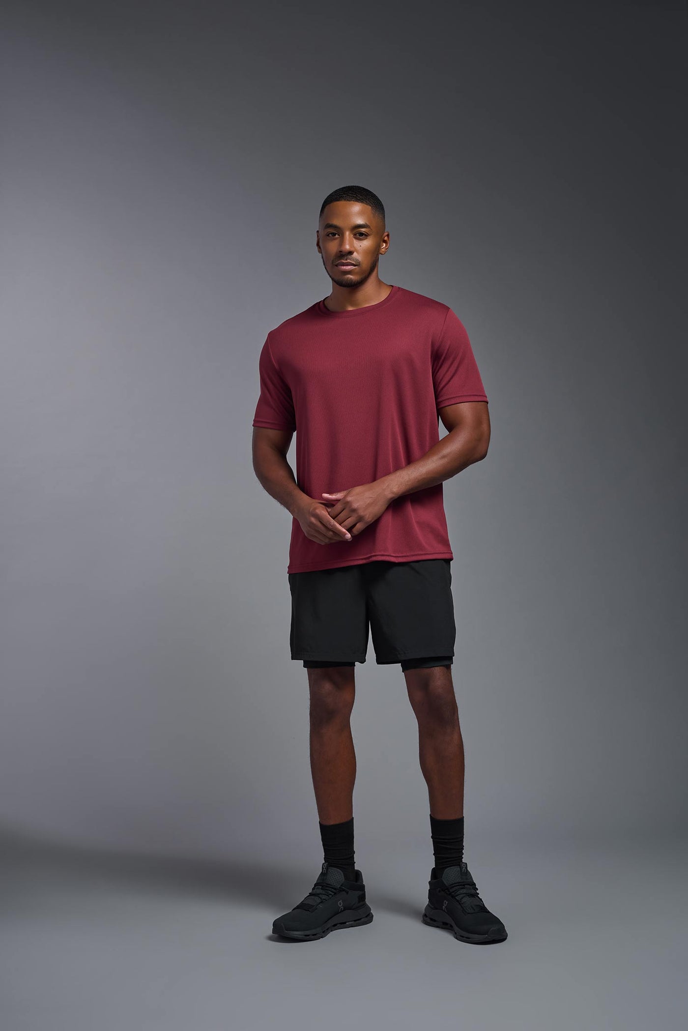 An African American male model with a beard on a gray background, wearing the Men's Oxymesh™ Crewneck Tech Tee in the color cardinal from a full body front view. This shirt is made in the USA and is quick-drying and moisture-wicking. #color_cardinal