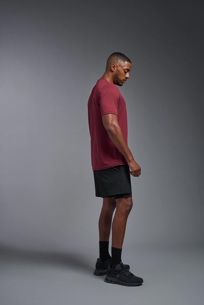 An African American male model with a beard on a gray background, wearing the Men's Oxymesh™ Crewneck Tech Tee in the color cardinal from a full body side view. This shirt is made in the USA and is quick-drying and moisture-wicking. #color_cardinal
