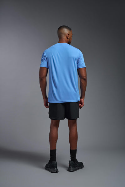 An African American male model with a beard on a gray background, wearing the Men's Oxymesh™ Crewneck Tech Tee in the color carolina blue from a full body back view. This shirt is made in the USA and is quick-drying and moisture-wicking. #color_carolina-blue