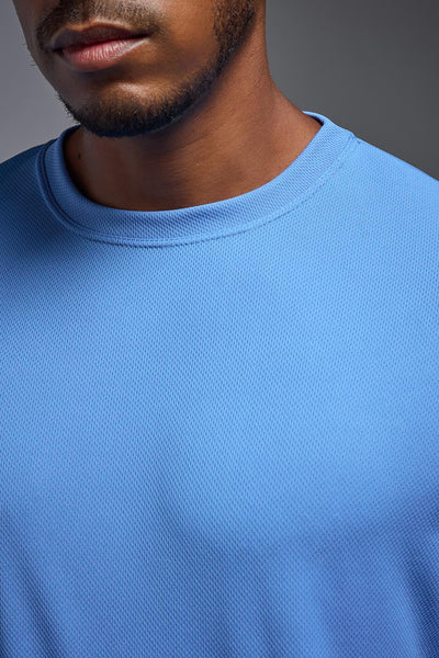 An African American male model with a beard on a gray background, wearing the Men's Oxymesh™ Crewneck Tech Tee in the color carolina blue from a closeup collar front view. This shirt is made in the USA and is quick-drying and moisture-wicking. #color_carolina-blue
