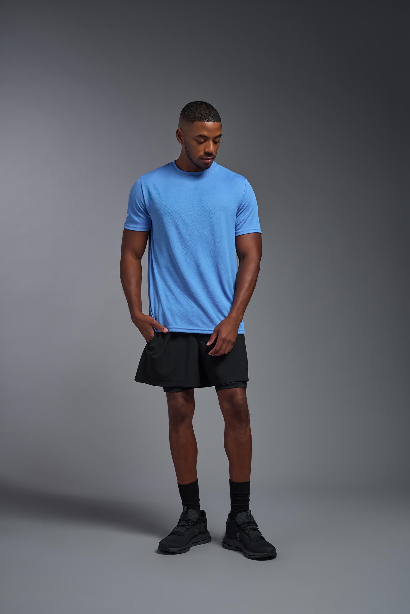 An African American male model with a beard on a gray background, wearing the Men's Oxymesh™ Crewneck Tech Tee in the color carolina blue from a full body front view. This shirt is made in the USA and is quick-drying and moisture-wicking. #color_carolina-blue