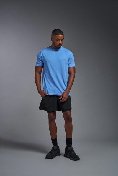 An African American male model with a beard on a gray background, wearing the Men's Oxymesh™ Crewneck Tech Tee in the color carolina blue from a full body front view. This shirt is made in the USA and is quick-drying and moisture-wicking. #color_carolina-blue