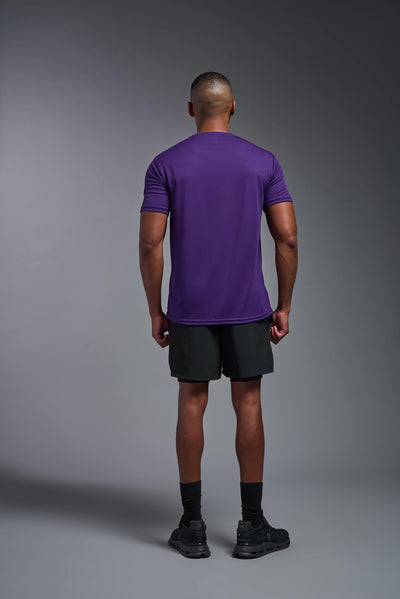 An African American male model with a beard on a gray background, wearing the Men's Oxymesh™ Crewneck Tech Tee in the color dark purple from a full body back view. This shirt is made in the USA and is quick-drying and moisture-wicking. #color_dark-purple