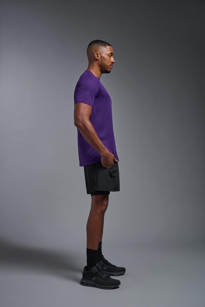 An African American male model with a beard on a gray background, wearing the Men's Oxymesh™ Crewneck Tech Tee in the color dark purple from a full body side view. This shirt is made in the USA and is quick-drying and moisture-wicking. #color_dark-purple