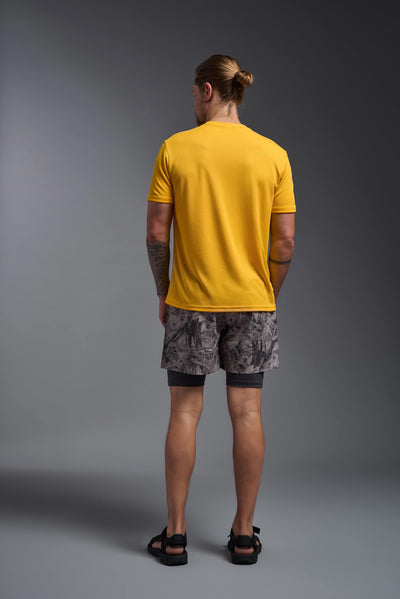 A blonde male model with a beard on a gray background, wearing the Men's Oxymesh™ Crewneck Tech Tee in the color gold from a full body back view. This shirt is made in the USA and is quick-drying and moisture-wicking. #color_gold