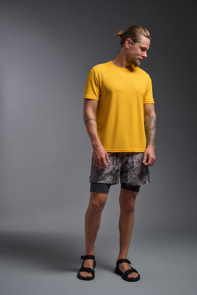 A blonde male model with a beard on a gray background, wearing the Men's Oxymesh™ Crewneck Tech Tee in the color gold from a full body front view. This shirt is made in the USA and is quick-drying and moisture-wicking. #color_gold