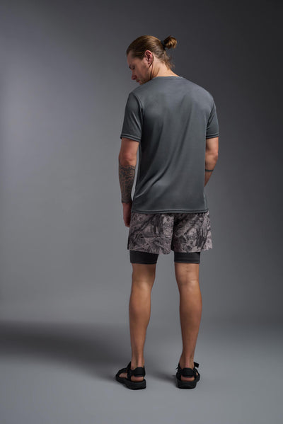 A blonde male model with a beard on a gray background, wearing the Men's Oxymesh™ Crewneck Tech Tee in the color graphite gray from a full body back view. This shirt is made in the USA and is quick-drying and moisture-wicking. #color_graphite-gray