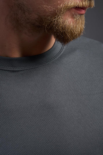A blonde male model with a beard on a gray background, wearing the Men's Oxymesh™ Crewneck Tech Tee in the color graphite gray from a closeup collar front view. This shirt is made in the USA and is quick-drying and moisture-wicking. #color_graphite-gray