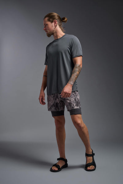 A blonde male model with a beard on a gray background, wearing the Men's Oxymesh™ Crewneck Tech Tee in the color graphite gray from a full body side view. This shirt is made in the USA and is quick-drying and moisture-wicking. #color_graphite-gray