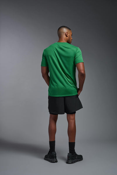 An African American male model with a beard on a gray background, wearing the Men's Oxymesh™ Crewneck Tech Tee in the color kelly green from a full body back view. This shirt is made in the USA and is quick-drying and moisture-wicking. #color_kelly-green