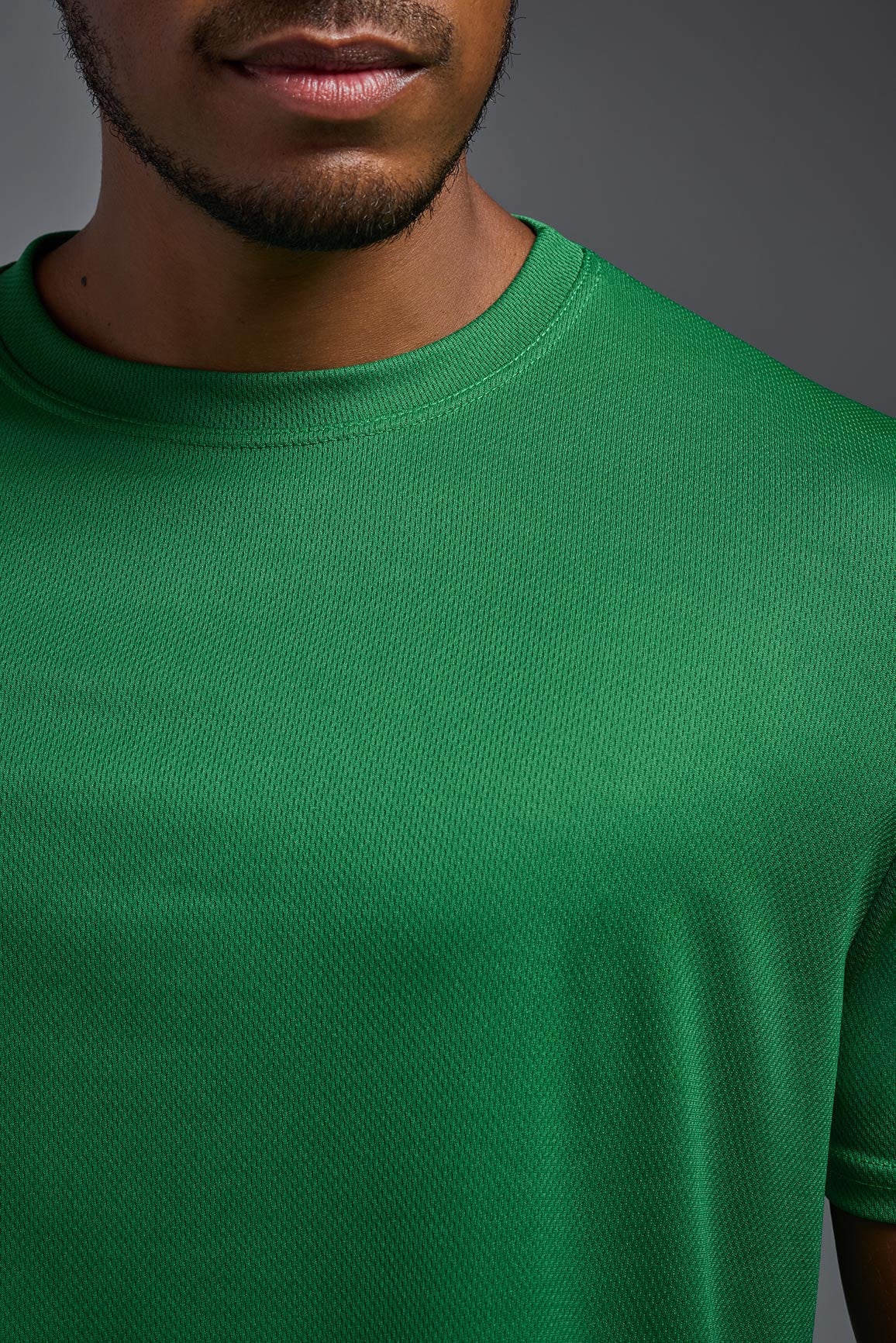 An African American male model with a beard on a gray background, wearing the Men's Oxymesh™ Crewneck Tech Tee in the color kelly green from a closeup collar front view. This shirt is made in the USA and is quick-drying and moisture-wicking. #color_kelly-green