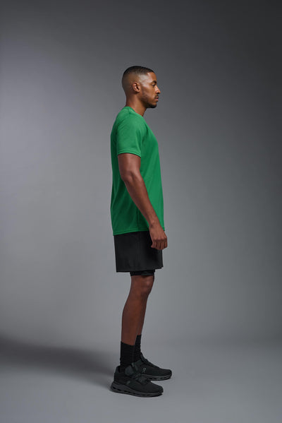 An African American male model with a beard on a gray background, wearing the Men's Oxymesh™ Crewneck Tech Tee in the color kelly green from a full body side view. This shirt is made in the USA and is quick-drying and moisture-wicking. #color_kelly-green