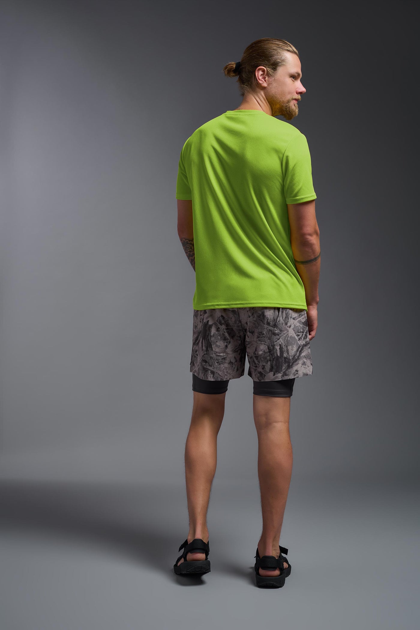 A blonde male model with a beard on a gray background, wearing the Men's Oxymesh™ Crewneck Tech Tee in the color key lime from a full body back view. This shirt is made in the USA and is quick-drying and moisture-wicking. #color_key-lime