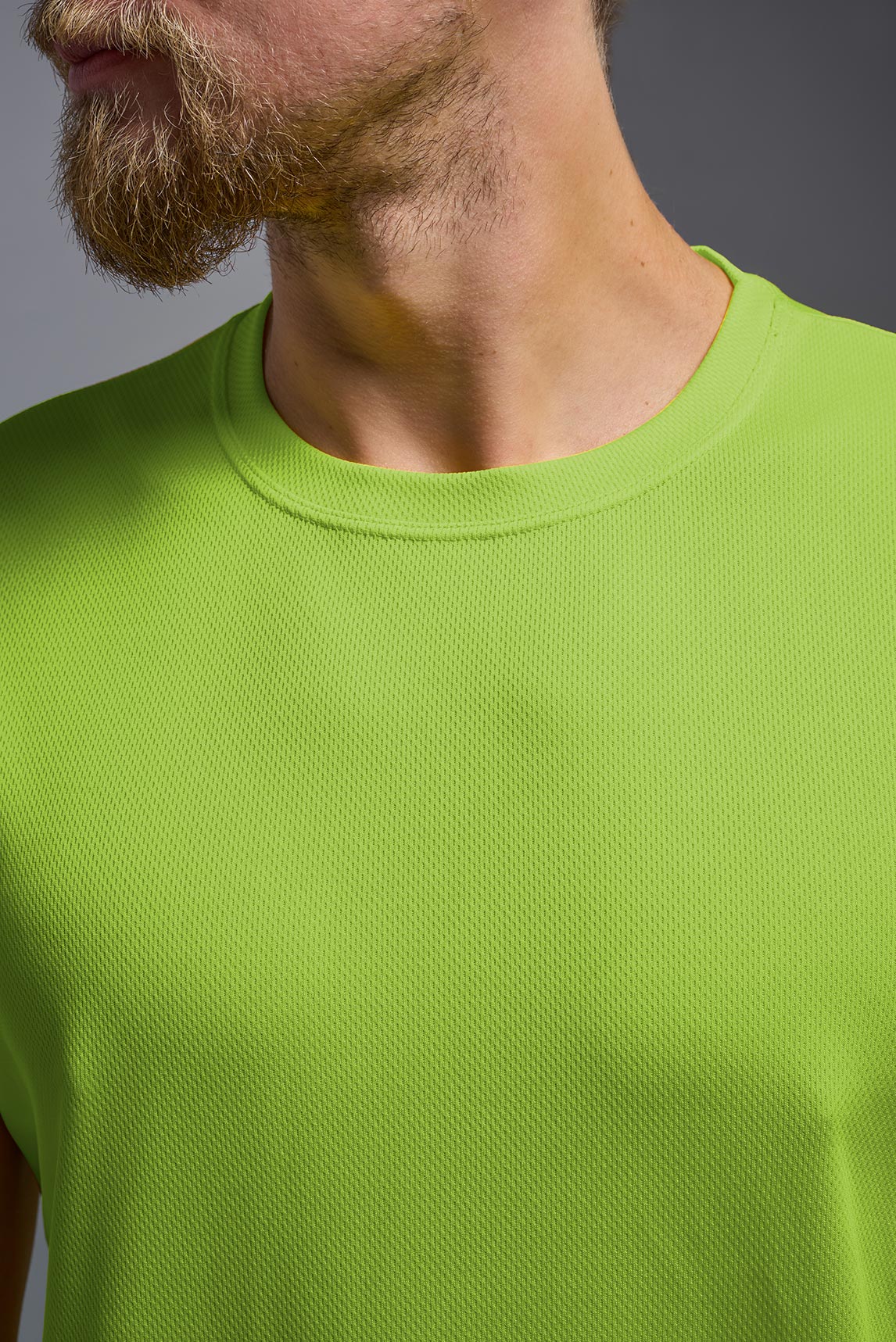 A blonde male model with a beard on a gray background, wearing the Men's Oxymesh™ Crewneck Tech Tee in the color key lime from a closeup collar front view. This shirt is made in the USA and is quick-drying and moisture-wicking. #color_key-lime