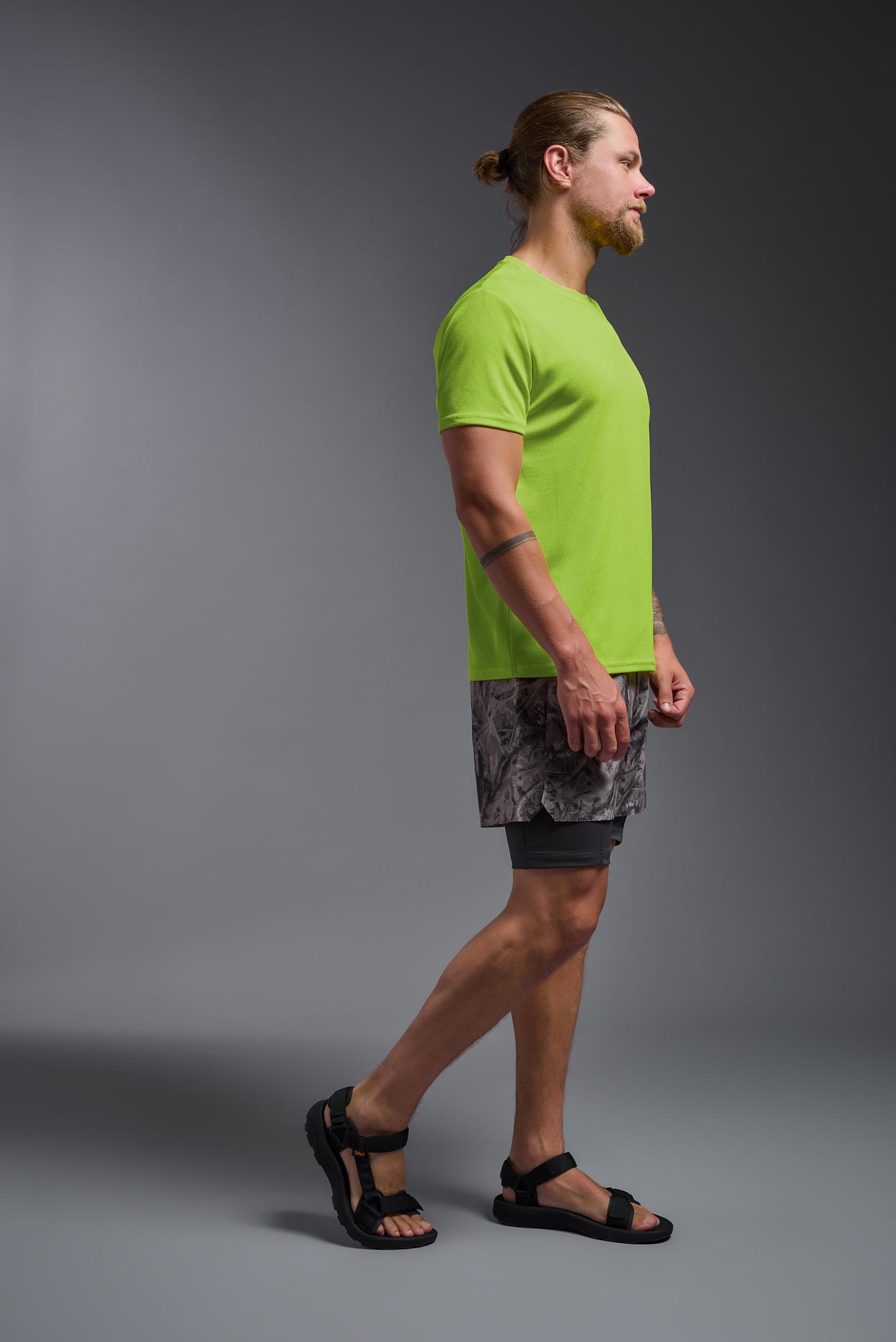 A blonde male model with a beard on a gray background, wearing the Men's Oxymesh™ Crewneck Tech Tee in the color key lime from a full body side view. This shirt is made in the USA and is quick-drying and moisture-wicking. #color_key-lime