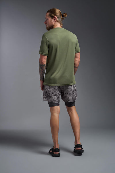 A blonde male model with a beard on a gray background, wearing the Men's Oxymesh™ Crewneck Tech Tee in the color military green from a full body back view. This shirt is made in the USA and is quick-drying and moisture-wicking. #color_military-green
