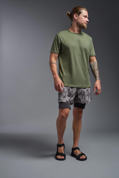 A blonde male model with a beard on a gray background, wearing the Men's Oxymesh™ Crewneck Tech Tee in the color military green from a full body front view. This shirt is made in the USA and is quick-drying and moisture-wicking. #color_military-green