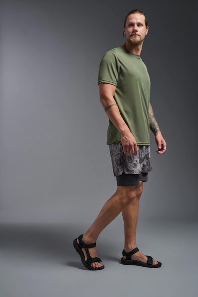 A blonde male model with a beard on a gray background, wearing the Men's Oxymesh™ Crewneck Tech Tee in the color military green from a full body side view. This shirt is made in the USA and is quick-drying and moisture-wicking. #color_military-green