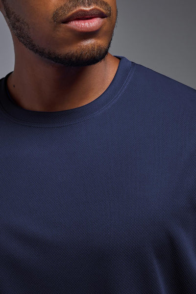 An African American male model with a beard on a gray background, wearing the Men's Oxymesh™ Crewneck Tech Tee in the color navy blue from a closeup collar front view. This shirt is made in the USA and is quick-drying and moisture-wicking. #color_navy-blue