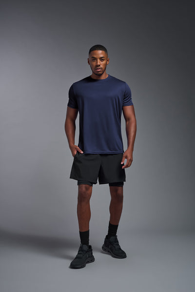 An African American male model with a beard on a gray background, wearing the Men's Oxymesh™ Crewneck Tech Tee in the color navy blue from a full body front view. This shirt is made in the USA and is quick-drying and moisture-wicking. #color_navy-blue