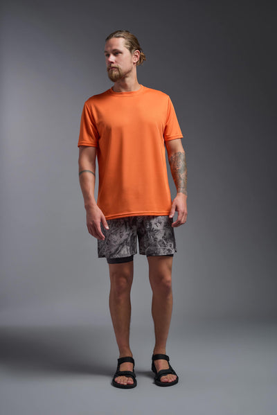A blonde male model with a beard on a gray background, wearing the Men's Oxymesh™ Crewneck Tech Tee in the color orange from a full body front view. This shirt is made in the USA and is quick-drying and moisture-wicking. #color_orange
