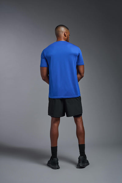 An African American male model with a beard on a gray background, wearing the Men's Oxymesh™ Crewneck Tech Tee in the color royal blue from a full body back view. This shirt is made in the USA and is quick-drying and moisture-wicking. #color_royal-blue
