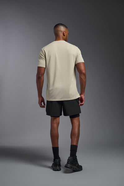 An African American male model with a beard on a gray background, wearing the Men's Oxymesh™ Crewneck Tech Tee in the color sand from a full body back view. This shirt is made in the USA and is quick-drying and moisture-wicking. #color_sand