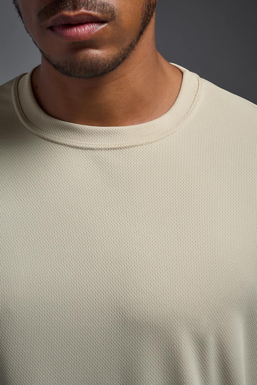 An African American male model with a beard on a gray background, wearing the Men's Oxymesh™ Crewneck Tech Tee in the color sand from a closeup collar front view. This shirt is made in the USA and is quick-drying and moisture-wicking. #color_sand