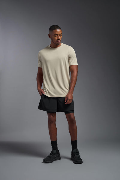 An African American male model with a beard on a gray background, wearing the Men's Oxymesh™ Crewneck Tech Tee in the color sand from a full body front view. This shirt is made in the USA and is quick-drying and moisture-wicking. #color_sand