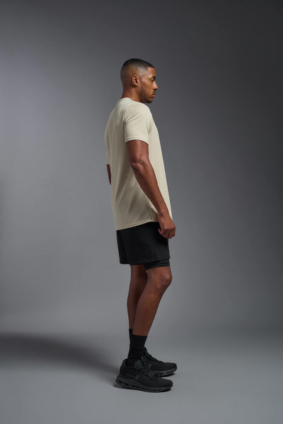 An African American male model with a beard on a gray background, wearing the Men's Oxymesh™ Crewneck Tech Tee in the color sand from a full body side view. This shirt is made in the USA and is quick-drying and moisture-wicking. #color_sand