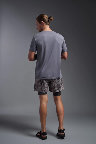 A blonde male model with a beard on a gray background, wearing the Men's Oxymesh™ Crewneck Tech Tee in the color steel gray from a full body back view. This shirt is made in the USA and is quick-drying and moisture-wicking. #color_steel-gray