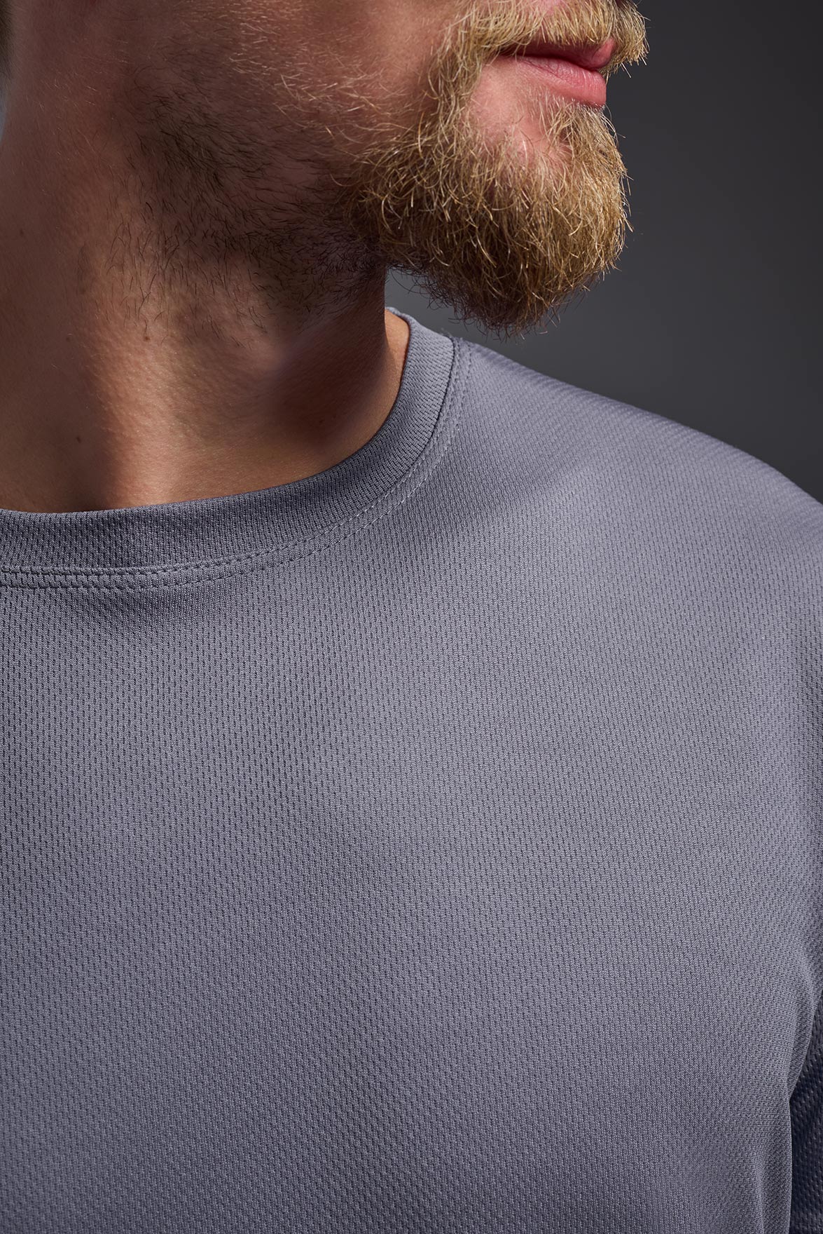 A blonde male model with a beard on a gray background, wearing the Men's Oxymesh™ Crewneck Tech Tee in the color steel gray from a closeup collar front view. This shirt is made in the USA and is quick-drying and moisture-wicking. #color_steel-gray