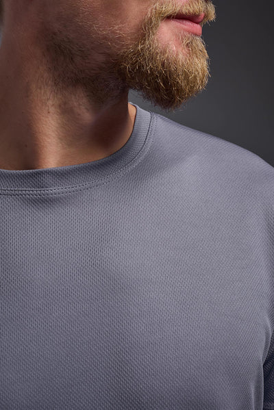 A blonde male model with a beard on a gray background, wearing the Men's Oxymesh™ Crewneck Tech Tee in the color steel gray from a closeup collar front view. This shirt is made in the USA and is quick-drying and moisture-wicking. #color_steel-gray