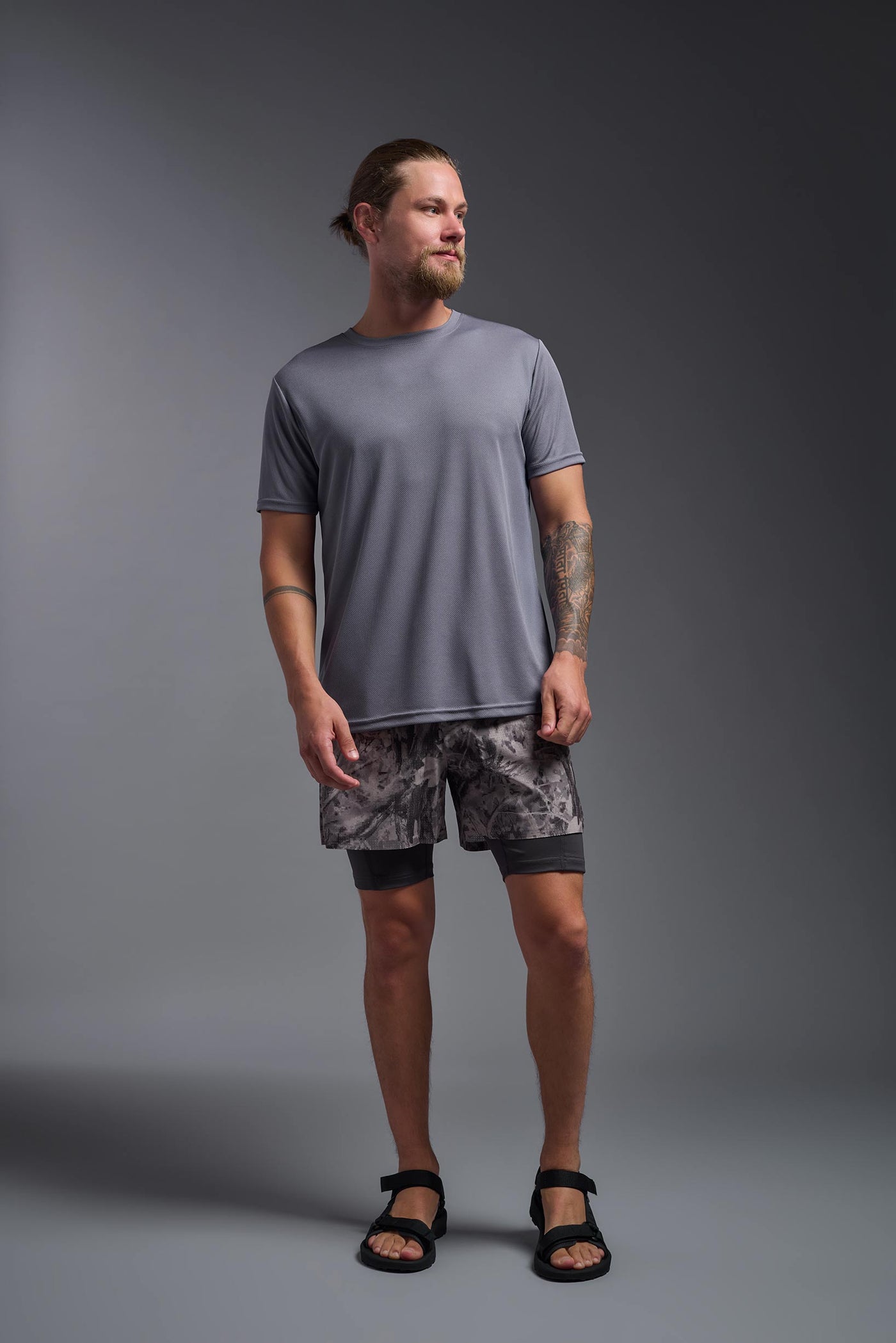 A blonde male model with a beard on a gray background, wearing the Men's Oxymesh™ Crewneck Tech Tee in the color steel gray from a full body front view. This shirt is made in the USA and is quick-drying and moisture-wicking. #color_steel-gray