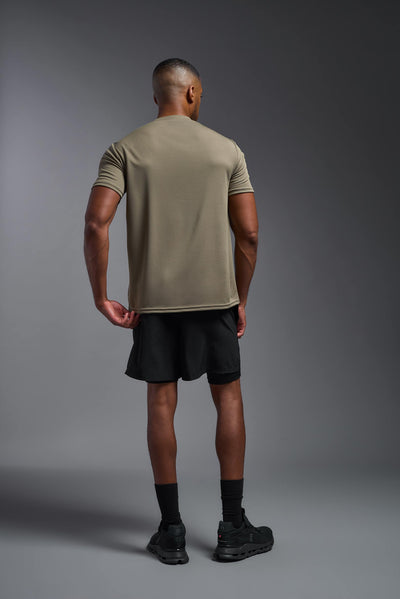 An African American male model with a beard on a gray background, wearing the Men's Oxymesh™ Crewneck Tech Tee in the color tan-499 from a full body back view. This shirt is made in the USA and is quick-drying and moisture-wicking. #color_tan-499