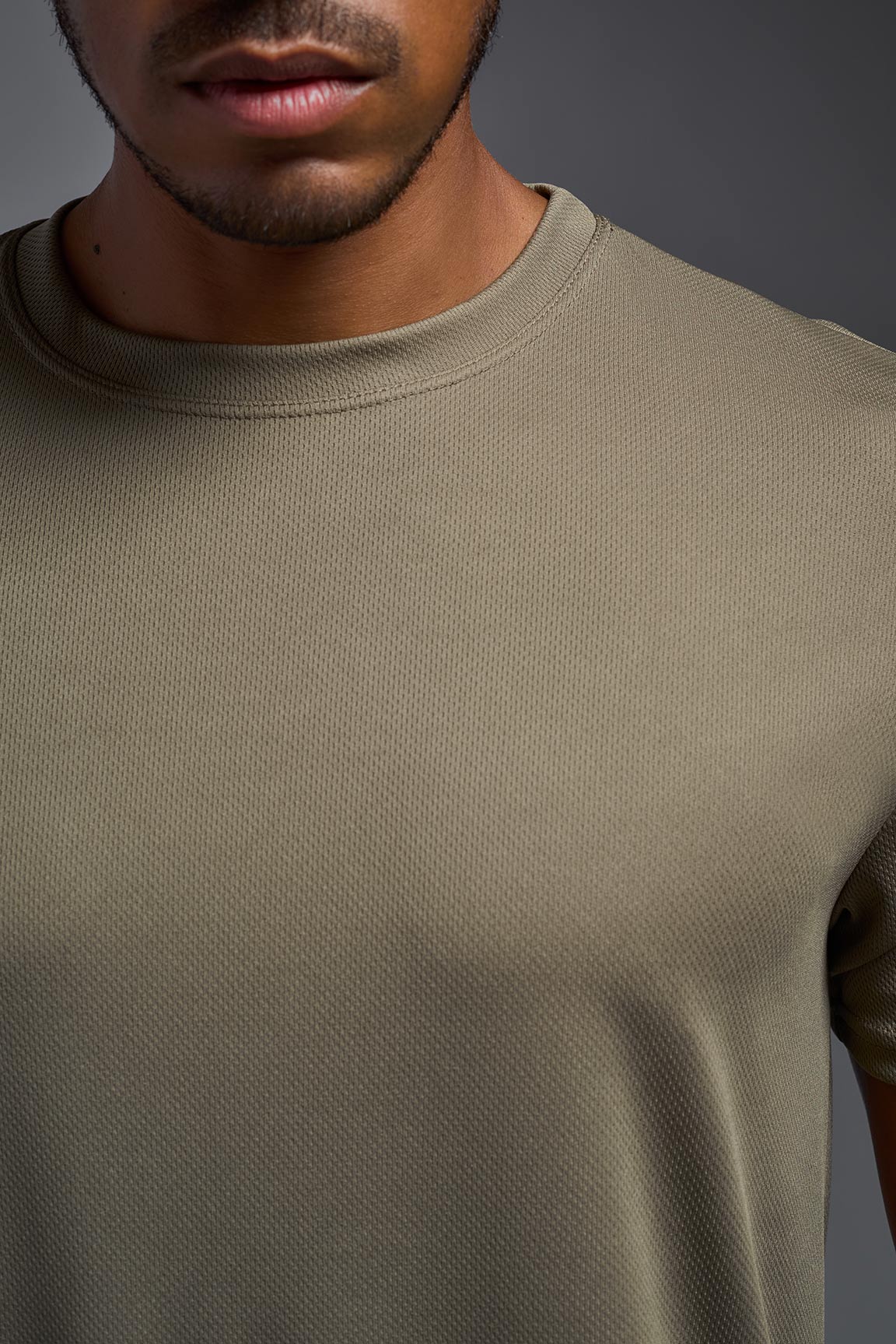 An African American male model with a beard on a gray background, wearing the Men's Oxymesh™ Crewneck Tech Tee in the color tan-499 from a closeup collar front view. This shirt is made in the USA and is quick-drying and moisture-wicking. #color_tan-499