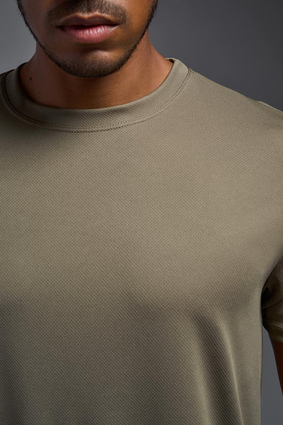 An African American male model with a beard on a gray background, wearing the Men's Oxymesh™ Crewneck Tech Tee in the color tan-499 from a closeup collar front view. This shirt is made in the USA and is quick-drying and moisture-wicking. #color_tan-499