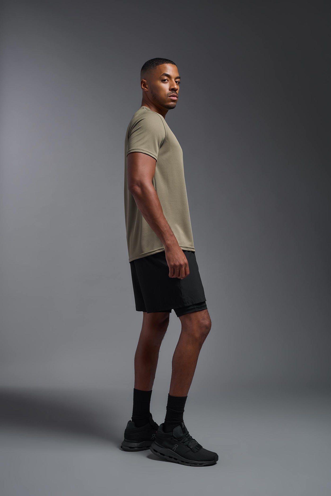 An African American male model with a beard on a gray background, wearing the Men's Oxymesh™ Crewneck Tech Tee in the color tan-499 from a full body side view. This shirt is made in the USA and is quick-drying and moisture-wicking. #color_tan-499