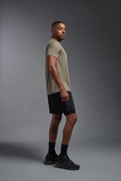 An African American male model with a beard on a gray background, wearing the Men's Oxymesh™ Crewneck Tech Tee in the color tan-499 from a full body side view. This shirt is made in the USA and is quick-drying and moisture-wicking. #color_tan-499