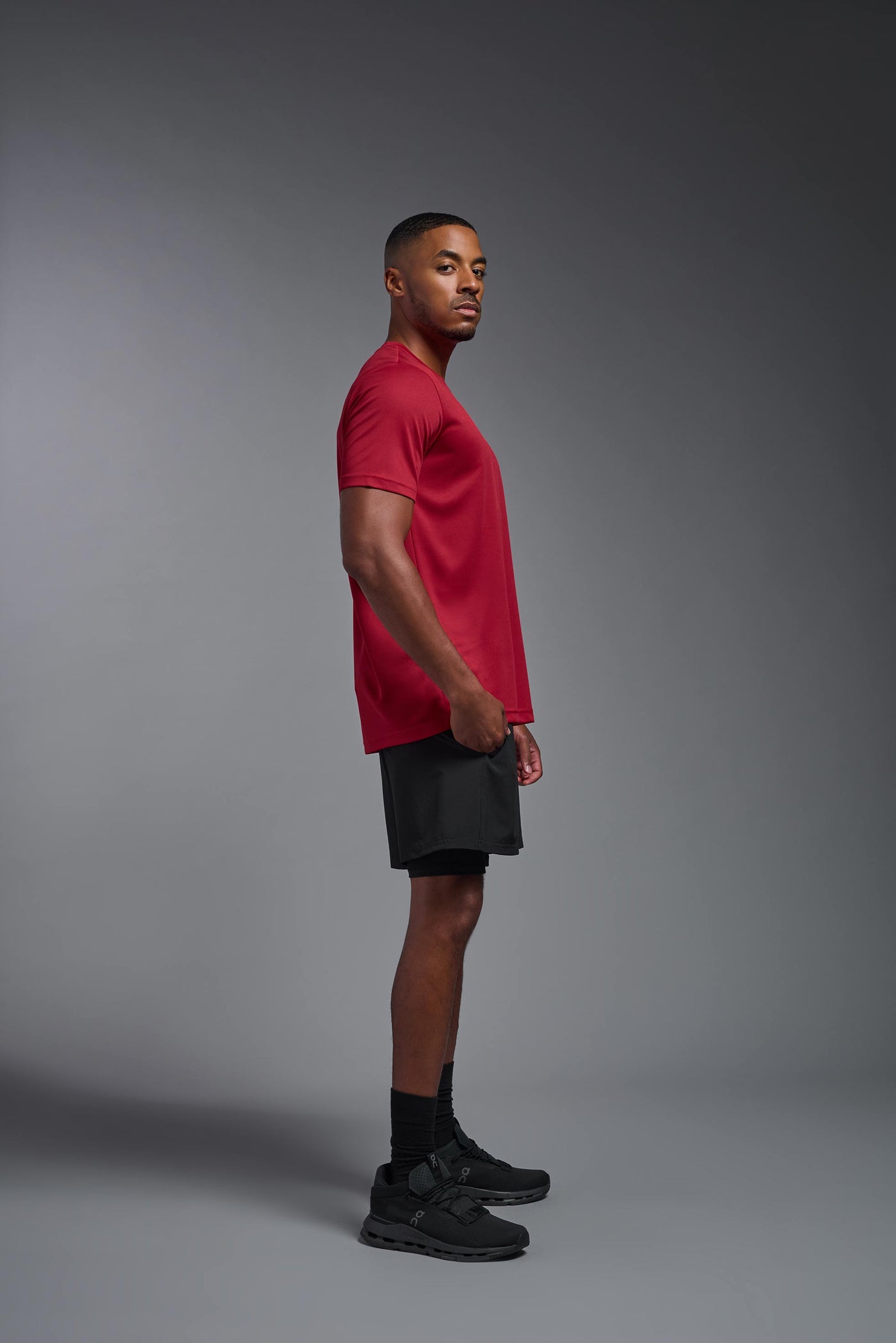 An African American male model with a beard on a gray background, wearing the Men's Oxymesh™ Crewneck Tech Tee in the color true red from a full body side view. This shirt is made in the USA and is quick-drying and moisture-wicking. #color_true-red