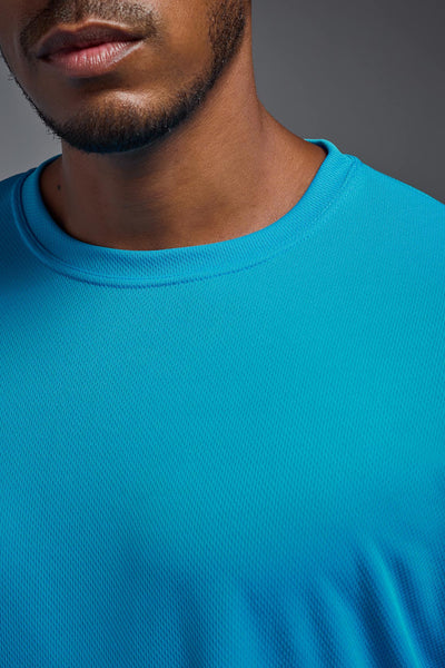 An African American male model with a beard on a gray background, wearing the Men's Oxymesh™ Crewneck Tech Tee in the color turquoise from a closeup collar front view. This shirt is made in the USA and is quick-drying and moisture-wicking. #color_turquoise