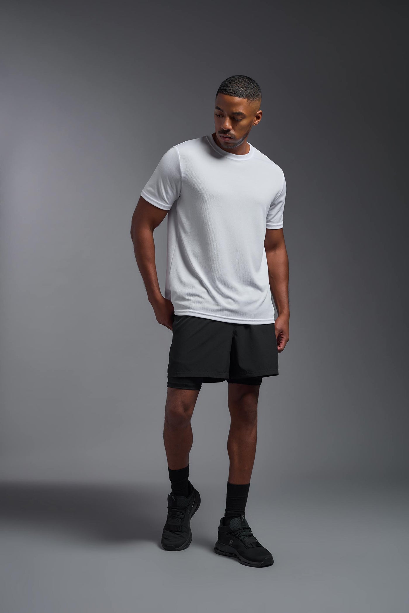 An African American male model with a beard on a gray background, wearing the Men's Oxymesh™ Crewneck Tech Tee in the color white from a full body front view. This shirt is made in the USA and is quick-drying and moisture-wicking. #color_white