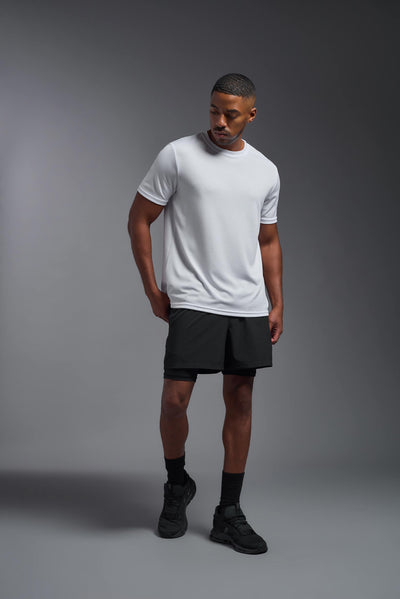 An African American male model with a beard on a gray background, wearing the Men's Oxymesh™ Crewneck Tech Tee in the color white from a full body front view. This shirt is made in the USA and is quick-drying and moisture-wicking. #color_white