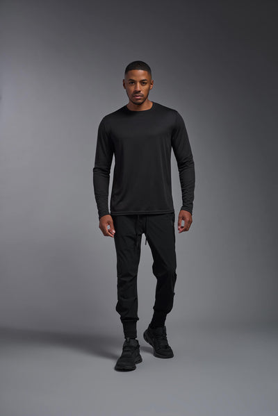 An African American male model with a beard wearing the men's Oxymesh Long Sleeve Tech Tee in the color black on a gray background, made out of 100% polyester, showing the relaxed fit from a full body front view. This shirt is breathable, quick-drying, moisture-wicking, and made in the USA. #color_black