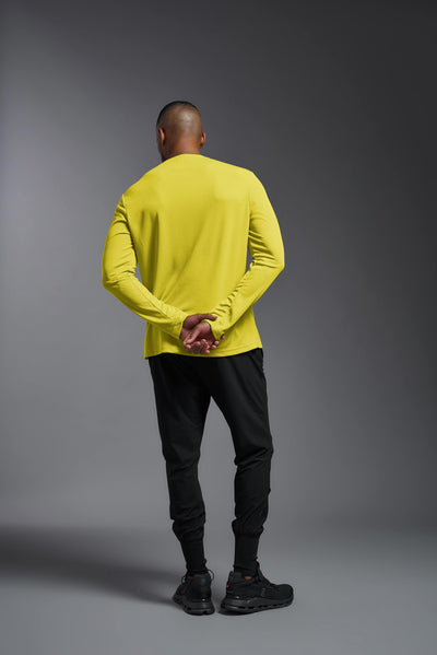 An African American male model with a beard wearing the men's Oxymesh Long Sleeve Tech Tee in the color bright yellow on a gray background, made out of 100% polyester, showing the relaxed fit from a full body front view. This shirt is breathable, quick-drying, moisture-wicking, and made in the USA. #color_bright-yellow