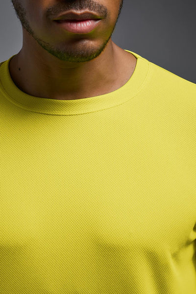 An African American male model with a beard wearing the men's Oxymesh Long Sleeve Tech Tee in the color bright yellow on a gray background, made out of 100% polyester, showing the relaxed fit from a closeup collar view. This shirt is breathable, quick-drying, moisture-wicking, and made in the USA. #color_bright-yellow