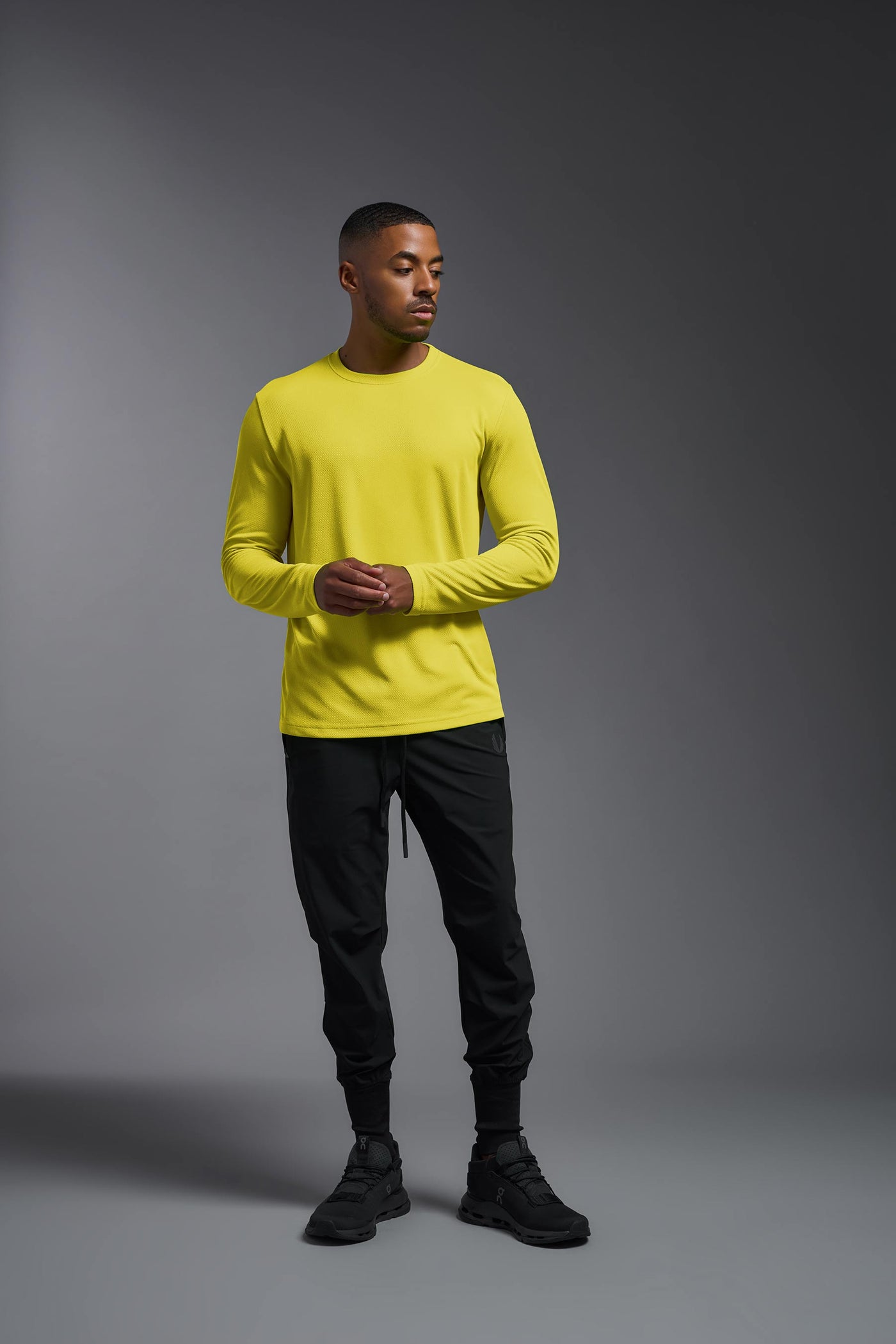 An African American male model with a beard wearing the men's Oxymesh Long Sleeve Tech Tee in the color bright yellow on a gray background, made out of 100% polyester, showing the relaxed fit from a full body front view. This shirt is breathable, quick-drying, moisture-wicking, and made in the USA. #color_bright-yellow